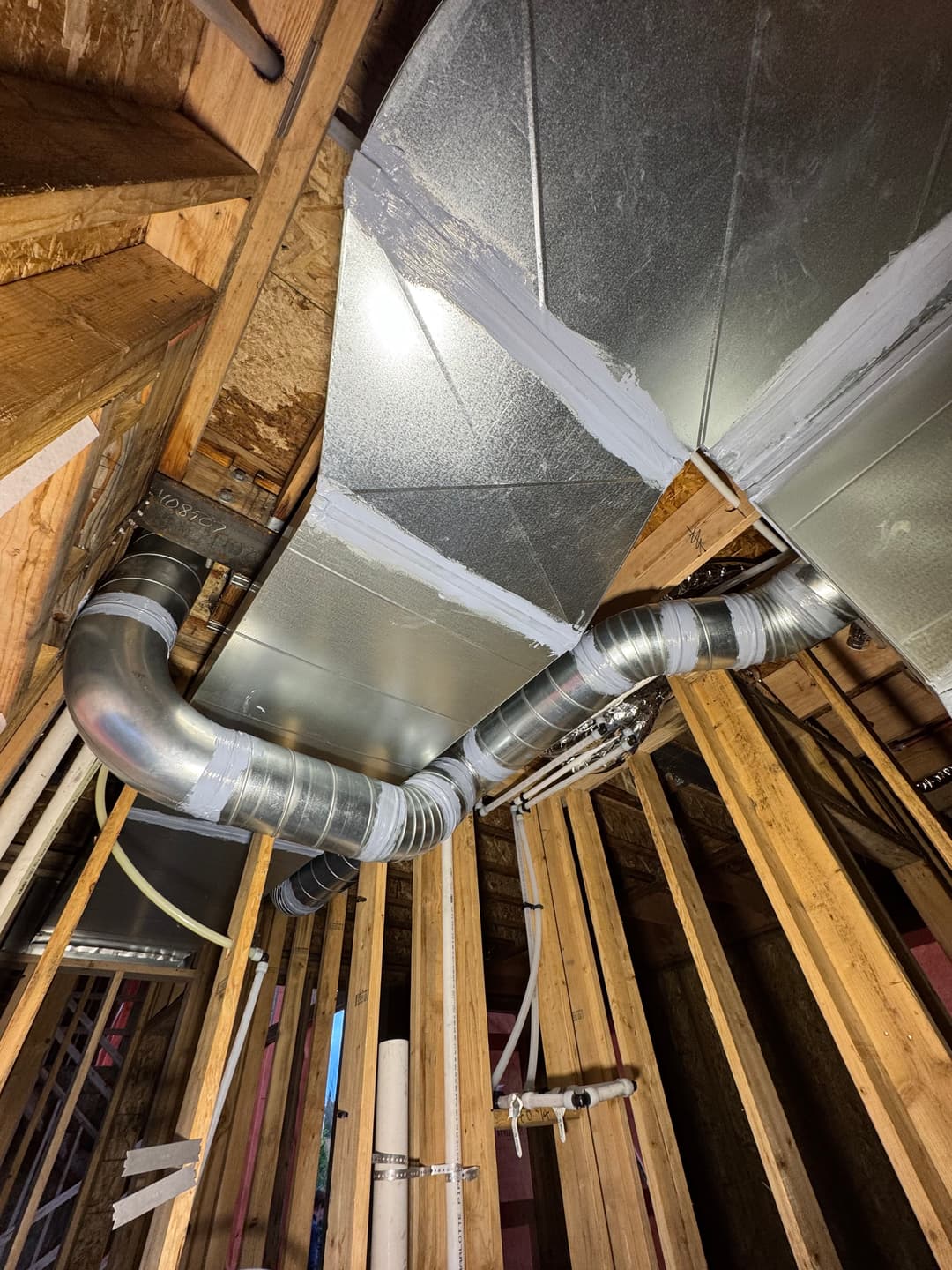 Ductwork installation in a wooden frame structure with metal and insulated tubing.