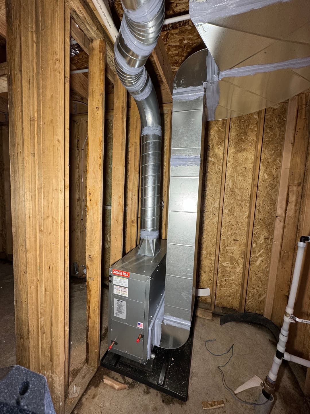 Furnace installation in a wooden framed basement with ductwork visible.