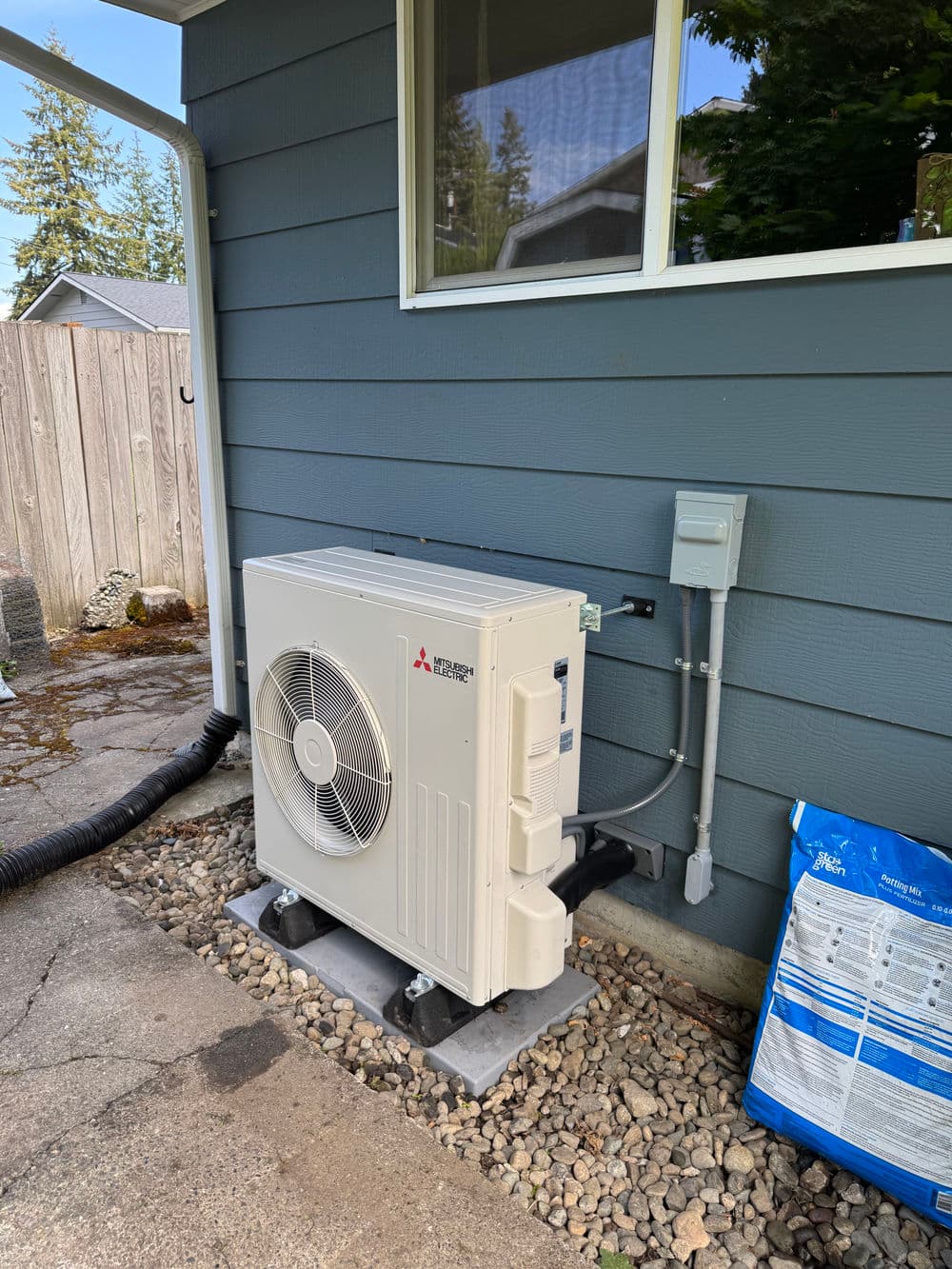 Mitsubishi outdoor air conditioning unit installed beside a house with gravel base.